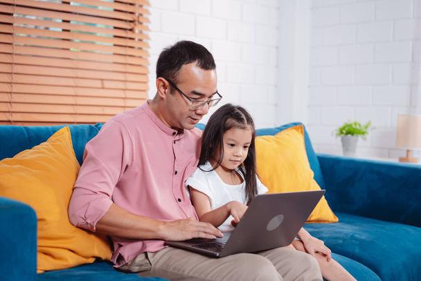 Cute little asian daughter with father working on laptop at home. single loving dad man shopping insurance to daughter by online technology. - 写真・画像