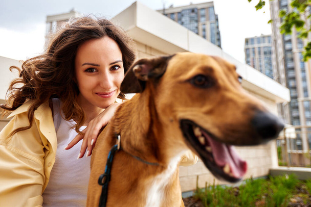Okouzlující mladá usměvavá dívka se psem zlaté barvy při procházce venku za slunečného dne. Ta holka objímá psa. Láska a náklonnost mezi majitelem a mazlíčkem. Selektivní zaměření, detailní záběr - Fotografie, Obrázek