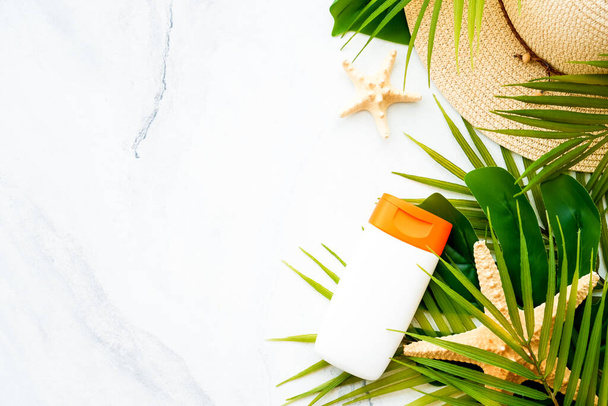 Concept vacances d'été. Crème solaire, feuilles de palmier et coquilles sur fond blanc. Pose plate avec espace de copie. - Photo, image