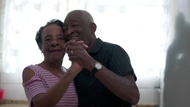 Ein fröhliches brasilianisches schwarzes Paar tanzt gemeinsam in der heimischen Küche. Afroamerikanische Rentner und Rentnerinnen Wange an Wange - Filmmaterial, Video