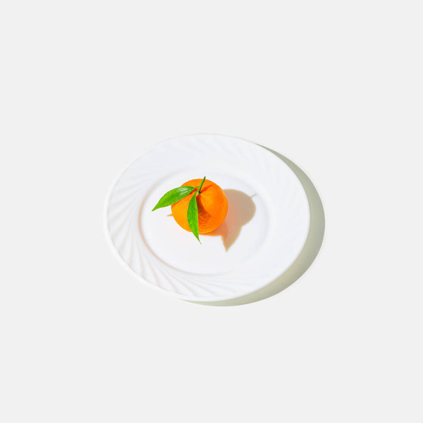 Creative still life composition made of fresh orange mandarin fruit on a plate on white background with shadow. Minimal style. Healthy food and vitamin concept. Summer refreshment theme. - Photo, Image