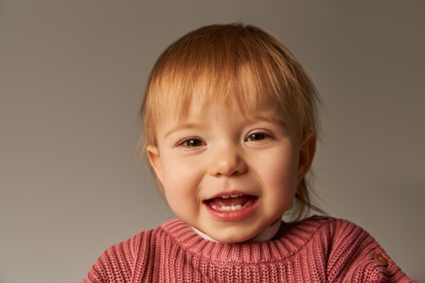 Portrait von niedlichen Baby-Mädchen, Kleinkind, glückliches kleines Kind in lässiger Kleidung lächelnd auf grauem Hintergrund im Studio, Emotionen, Unschuld, Kleinkind-Mode, stilvolles Outfit, rosa Pullover, Babygesicht - Foto, Bild