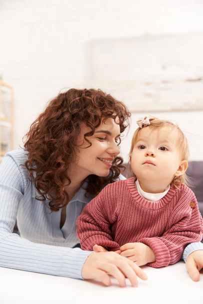 portrait of cheerful woman and child, curly working mother hugging baby girl, balanced lifestyle, bonding, happy family time, modern parenting, engaging with kid, loving motherhood  - 写真・画像