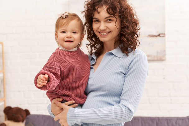 quality family time, working mother with curly hair holding in arms baby girl, woman and her toddler daughter, modern parenting, work life harmony, bonding and engaging with kid, happiness  - Foto, Imagen