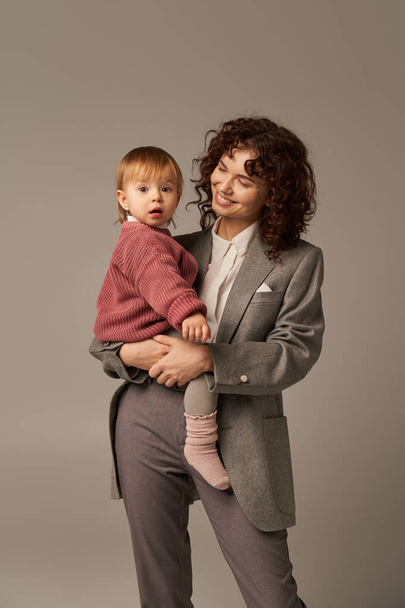 career and family, happy young woman holding in arms baby girl, balancing between work and life, modern parenting, businesswoman, mother daughter bond, lifestyle, grey background  - 写真・画像
