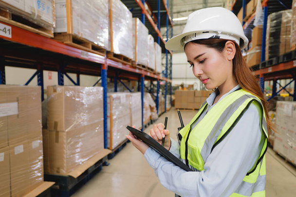 Warehouse manager in white helmet using tablet checking goods and supplies on shelves with goods background at warehouse factory, Logistic and business export concept - Zdjęcie, obraz