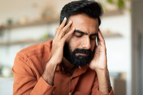 Headache And Stress. Upset Indian Man Touching Temples While Sitting On Couch At Home, Upset Young Bearded Guy Suffering From Headache Pain, Having Depression Or Feeling Unwell, Closeup Portrait - Fotoğraf, Görsel