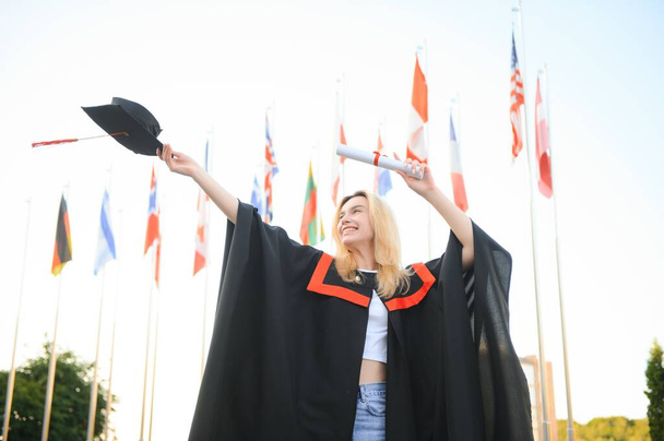 Happy university graduate girl. The girl is standing near the university against the background of the flags of different countries. The concept of international education - Fotografie, Obrázek
