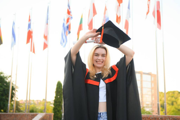 Happy university graduate girl. The girl is standing near the university against the background of the flags of different countries. The concept of international education - Photo, image