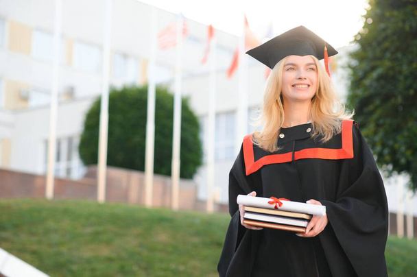Portrait enthusiastic female college student graduate in cap and gown celebrating, holding diploma - Valokuva, kuva