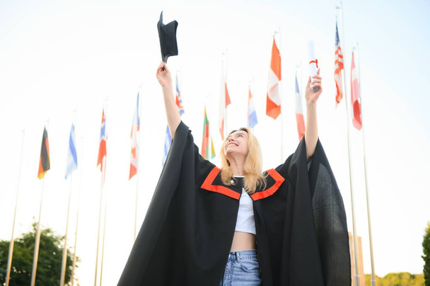 Portrait enthusiastic female college student graduate in cap and gown celebrating, holding diploma - Fotó, kép