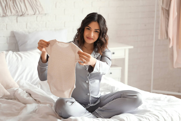 Young pregnant woman with baby bodysuit sitting in bedroom - Photo, Image