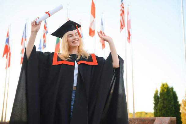 Happy university graduate girl. The girl is standing near the university against the background of the flags of different countries. The concept of international education - Φωτογραφία, εικόνα