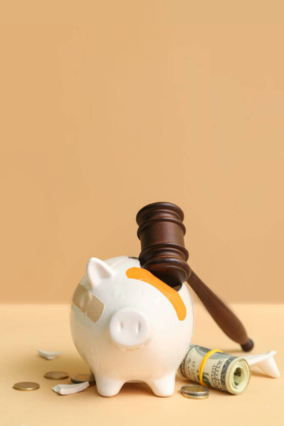 Broken patched piggy bank with judge gavel and money on orange background. Bankruptcy concept - 写真・画像
