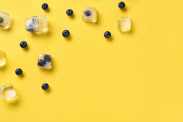 Bleuets mûrs congelés dans des glaçons et des baies fraîches sur fond jaune - Photo, image