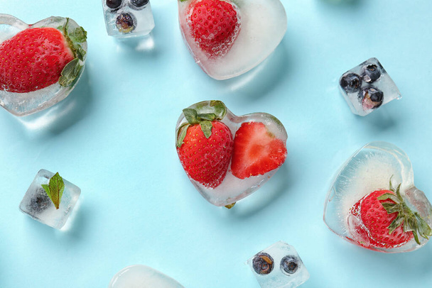 Čerstvé jahody a borůvky zmrazené v ledu na modrém pozadí - Fotografie, Obrázek
