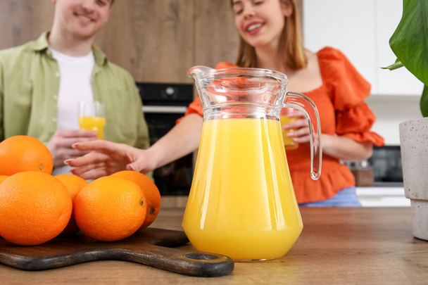 Jug of juice with oranges on table in kitchen, closeup - Photo, Image