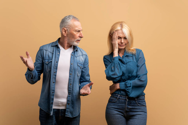 Psychological violence. Mature family couple experience marriage crisis, relationship problems. Angry irritated jealous old age husband abuser scold stressed upset senior wife, beige background - Foto, Imagem