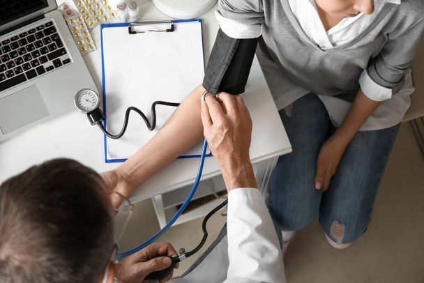 Reifer männlicher Arzt misst Blutdruck des Patienten in der Klinik, Nahaufnahme - Foto, Bild