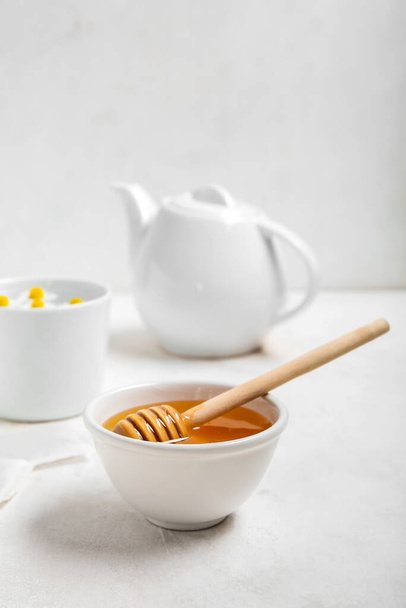Bowl of honey, teapot and cup with chamomile flowers on light background - Photo, Image