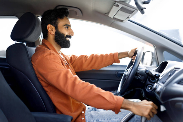 Propio auto. Vista lateral del alegre hombre de Oriente Medio conduciendo cómodo auto sentado en el lujoso interior del automóvil. Guapo barbudo hombre de negocios que va a la oficina en automóvil - Foto, imagen