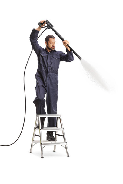 Man in a uniform using a pressure washer and standing on a ladder isolated on white background - Фото, зображення