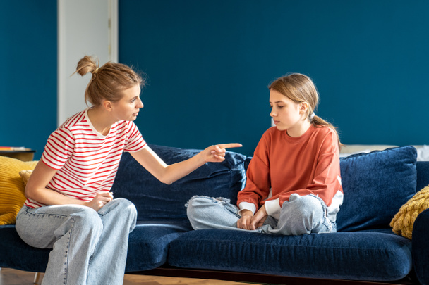 Angry mother pointing upset child sitting on sofa in living room. Conflict children and parents.Toxic mom humiliates young girl for bad behavior. Difficulties in raising teenage daughter - Zdjęcie, obraz