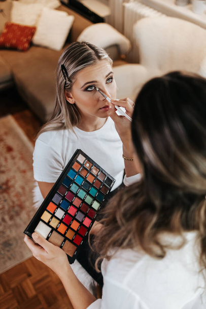 Makeup process. Professional artist applying make up on model face. Close up portrait of beautiful blonde woman in beauty salon.  - Фото, зображення