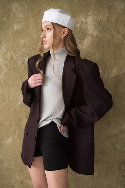 jong mooi blond model in een zwart pak en beige jas op een beige achtergrond  - Foto, afbeelding