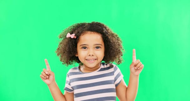 Face smile, girl child and pointing up on green screen in studio isolated on a background. Portrait, emoji and happy kid with hand gesture for mockup, advertising or marketing, branding or chroma key. - Photo, Image