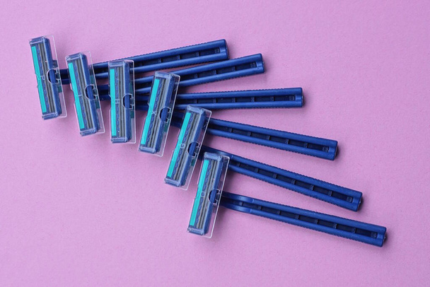 een set van zes blauwe plastic scheermesjes liggen op een roze tafel - Foto, afbeelding