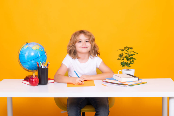 Egy sárga stúdió hátterű iskolás fiú portréja. Vissza a suliba. Vicces kisgyerek az általános iskolából könyvvel. Oktatás. Gyerek tanulás és tanulás - Fotó, kép