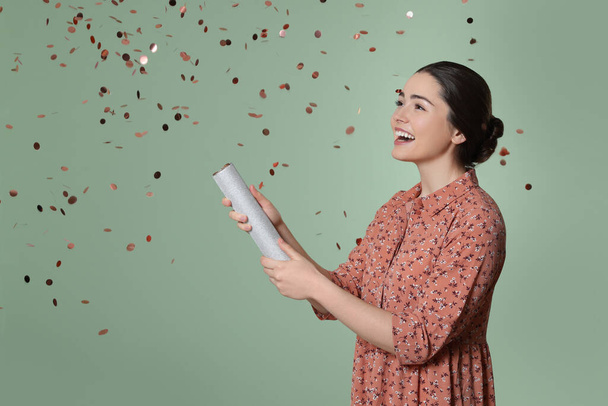 Young woman blowing up party popper on pale green background - Photo, Image