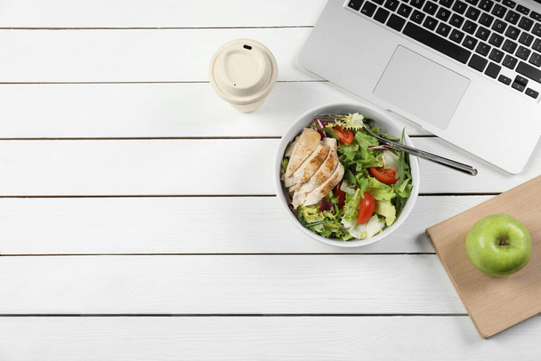 Bowl of tasty food, paper cup of coffee, laptop, apple and book on white wooden table, flat lay with space for text. Business lunch - Zdjęcie, obraz