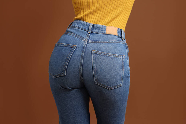 Woman in stylish jeans on brown background, closeup - Zdjęcie, obraz