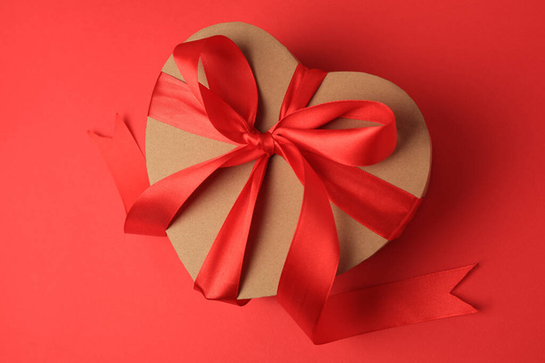 Beautiful heart shaped gift box with bow on red background, top view - Valokuva, kuva