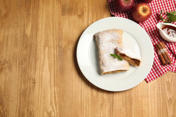 Delicious strudel with apples, nuts and raisins on wooden table, flat lay. Space for text - Foto, Imagen