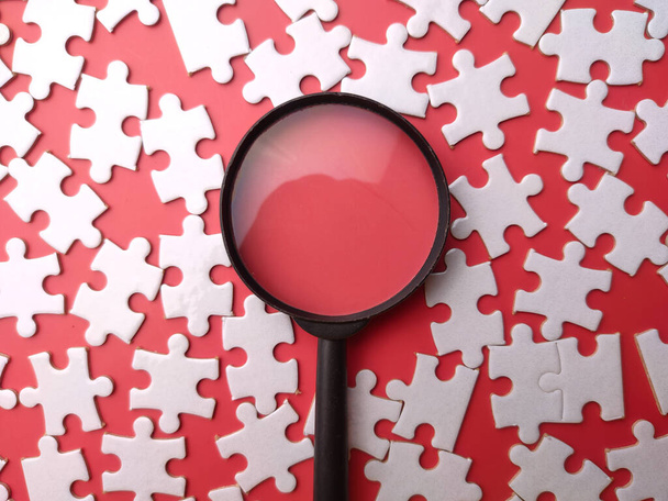 Weißes Puzzle und Lupe von oben auf rotem Hintergrund. - Foto, Bild