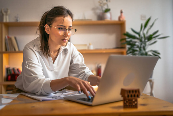 молода біла жінка навчається перед портативним комп'ютером вдома - жінка читає книгу, готує іспит або тест на призначення, що має онлайн-консультацію - концепцію освіти та навчання
 - Фото, зображення