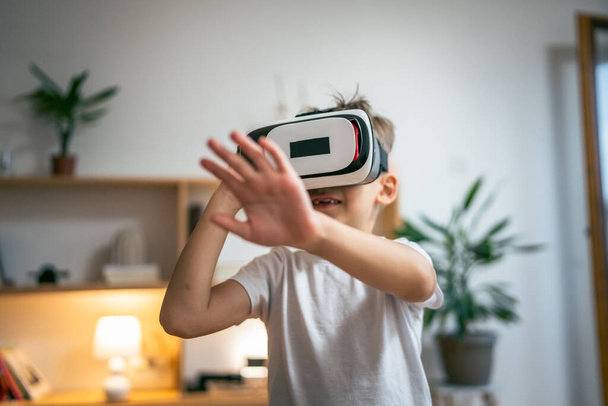 αγόρι αρσενικό καυκάσιο παιδί στο σπίτι απολαμβάνουν εικονική πραγματικότητα VR ακουστικά - Φωτογραφία, εικόνα