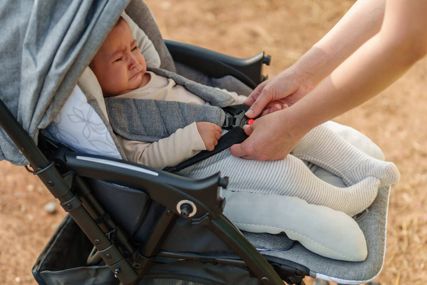 woman fastening belt on the stroller with crying baby - Foto, Imagem