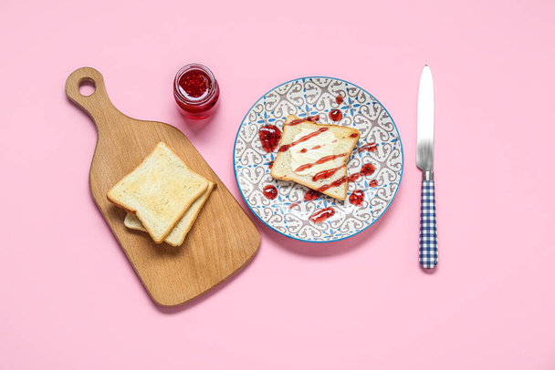 Plate with toast and jar of jam on pink background - Foto, afbeelding
