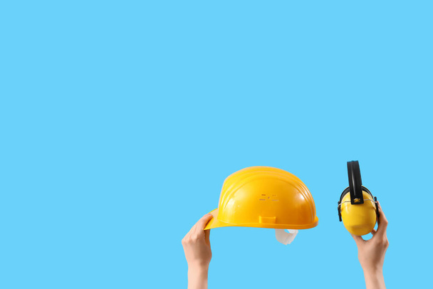 Female hands holding safety hardhat and ear muffs on blue background - Photo, Image