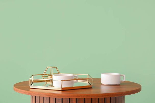 Holztisch mit Tablett und Tassen in der Nähe der grünen Wand - Foto, Bild