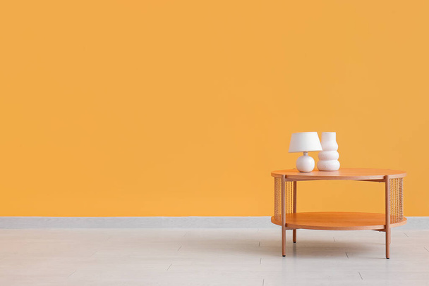 Drewniany stolik kawowy z lampą i pustym wazonem przy pomarańczowej ścianie - Zdjęcie, obraz