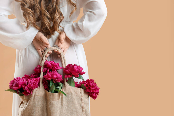Young woman with eco bag and peony flowers on beige background, back view - Foto, Imagem