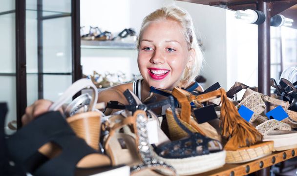 Young cheerful smiling girl choosing pair of shoes in boutique . - Foto, imagen