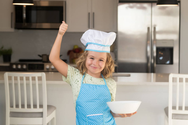 Criança cozinheiro chef com prato de cozinha. Engraçado cozinheiro miúdo cozinheiro vestindo uniforme cozinheiro cap e avental comida cozida na cozinha. As crianças estão preparando a massa, assar biscoitos na cozinha - Foto, Imagem