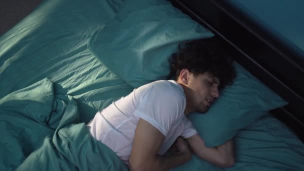 Gereizter junger Mann, der nachts im Bett liegt, an Schlaflosigkeit leidet, seinen Kopf mit einem Kopfkissen vor Lärm bedeckt, schlafloser Typ. Kopierraum - Filmmaterial, Video