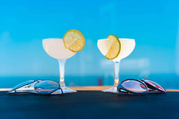 Two glasses of tasty white drink cocktails on wooden table.Blue sky,sea,summer evening. - Fotoğraf, Görsel